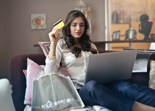 A woman holding a credit card and a laptop to buy online gifts.